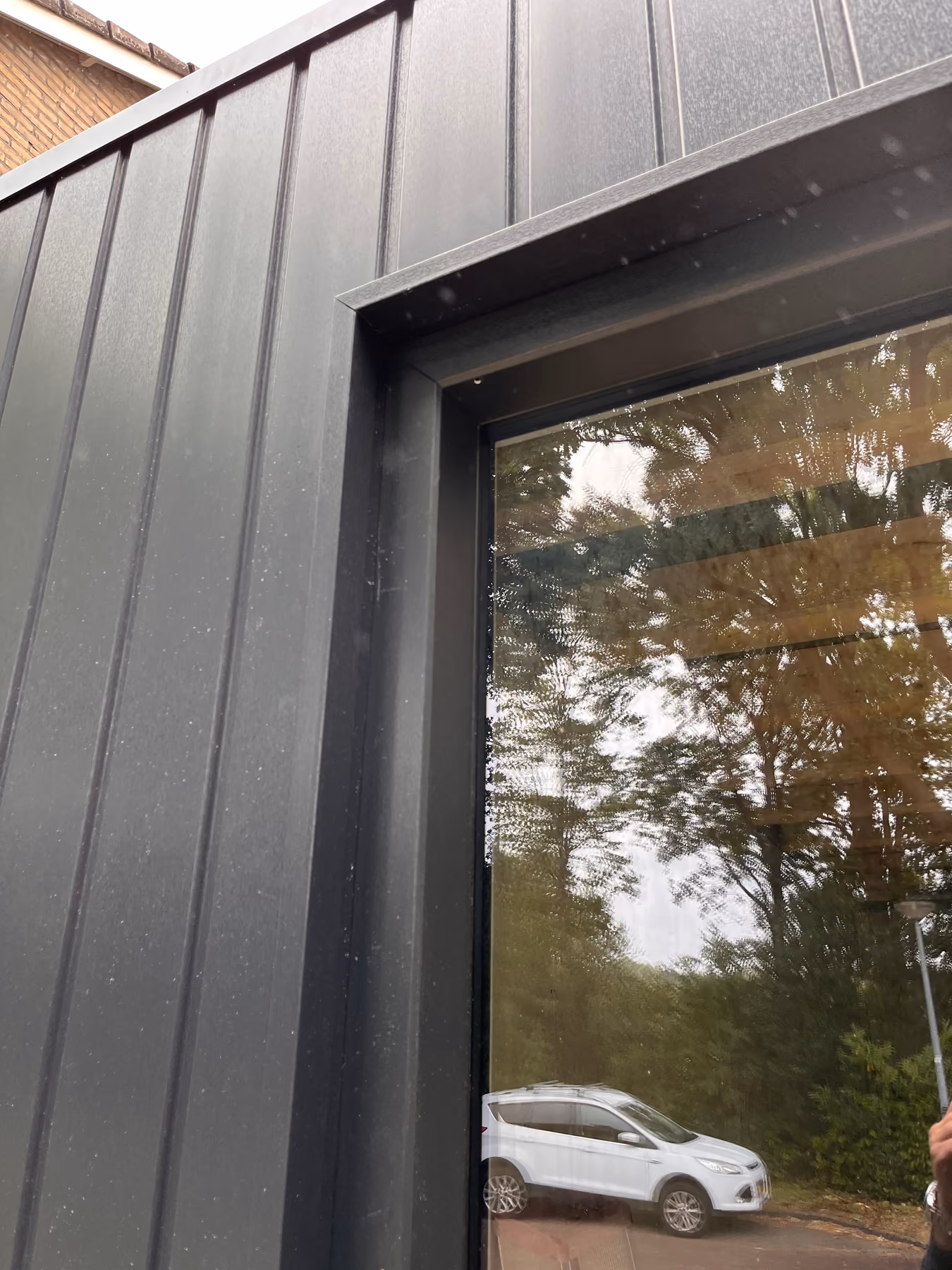 Close-up van donkere gevelbekleding rond een zwart kozijn met regendruppels