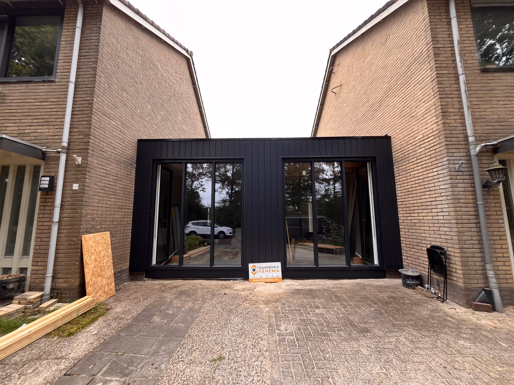 Afgeronde aanbouw met zwarte gevelbekleding en twee grote glazen puien