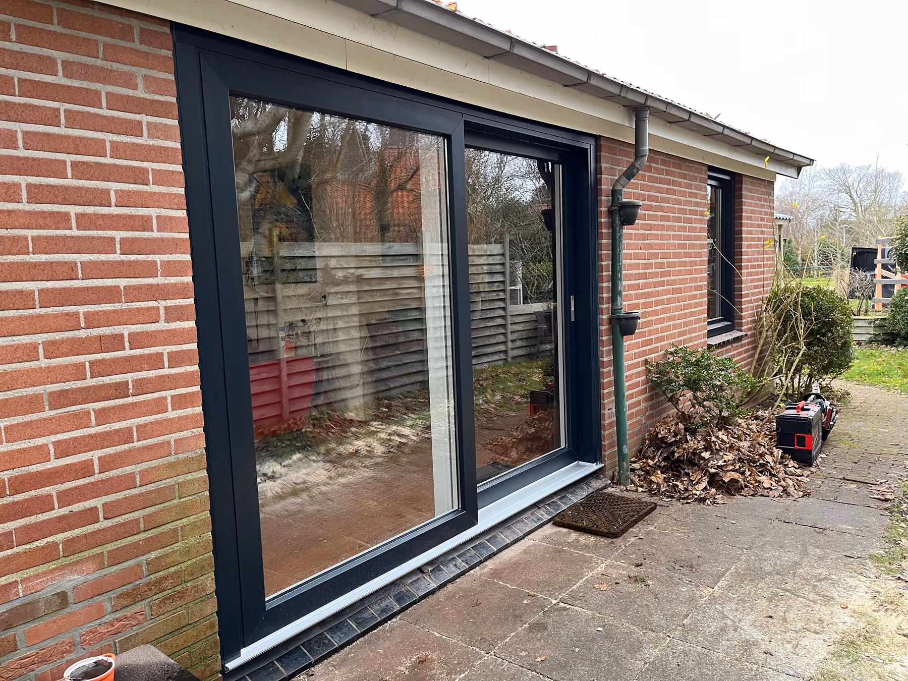 Grote antracieten schuifpui in de bakstenen gevel van een bungalow