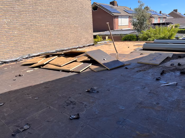 Plat dak met losgehaalde dakbedekking en gestapelde isolatieplaten tegen de zijgevel