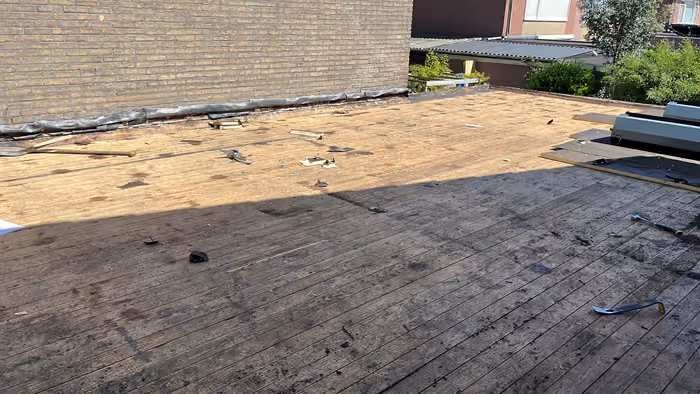 Plat dak gestript tot op het houten dakbeschot naast een gemetselde zijgevel