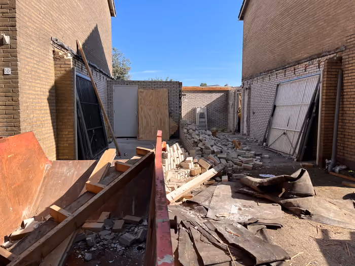 Sloopwerk tussen twee woningen met puin, oude dakbedekking en een container