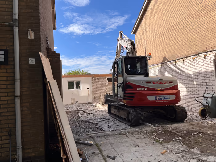 Rupskraan op het sloopterrein tussen twee woningen, gebroken bestrating en puin