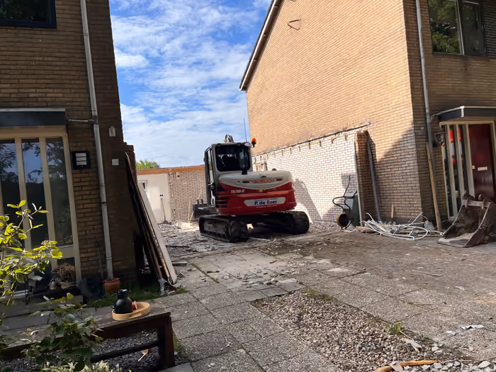 Graafmachine tussen twee woningen tijdens het opruimen van de oude aanbouw