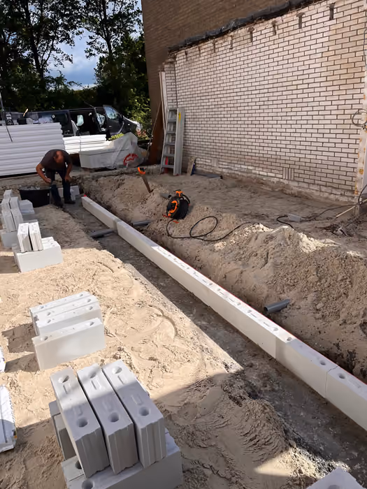 Vakman legt lichte bouwblokken op de fundering, stapels blokken in het zand