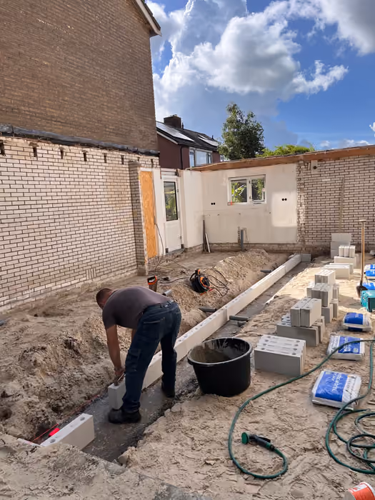Timmerman plaatst bouwblokken langs de nieuwe fundering naast de bestaande achtergevel
