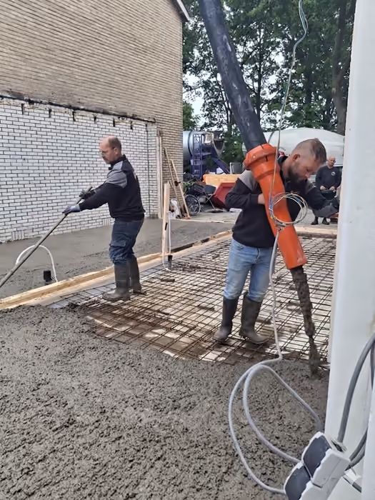 Twee vakmensen storten en verdichten beton op het wapeningsnet van de vloer
