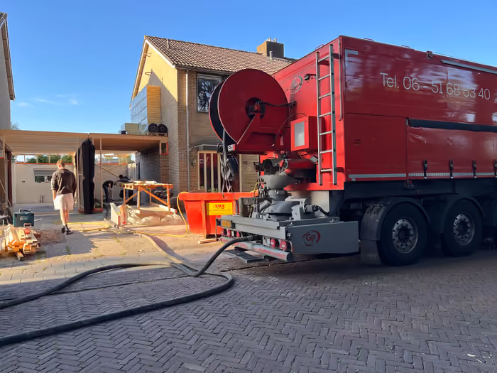 Rode vrachtwagen met slanghaspel levert via een slang materiaal bij de woning