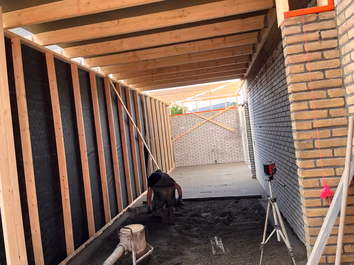 Werkman vlakt de dekvloer af in het houten casco van de aanbouw