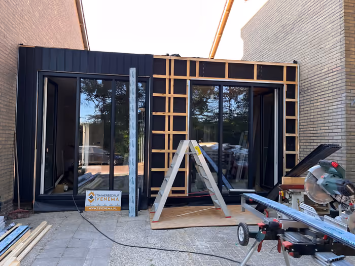 Donkere gevelbekleding half aangebracht op de aanbouw met grote zwarte kozijnen