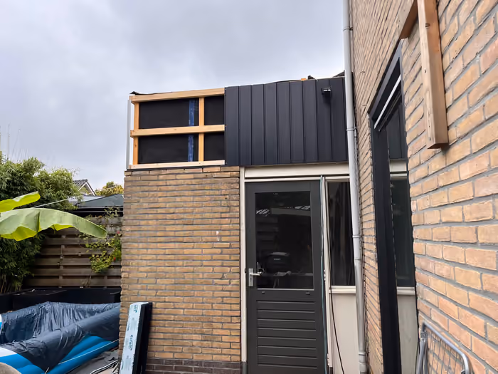Bovenbouw van de aanbouw met donkere gevelbekleding en open houten regelwerk