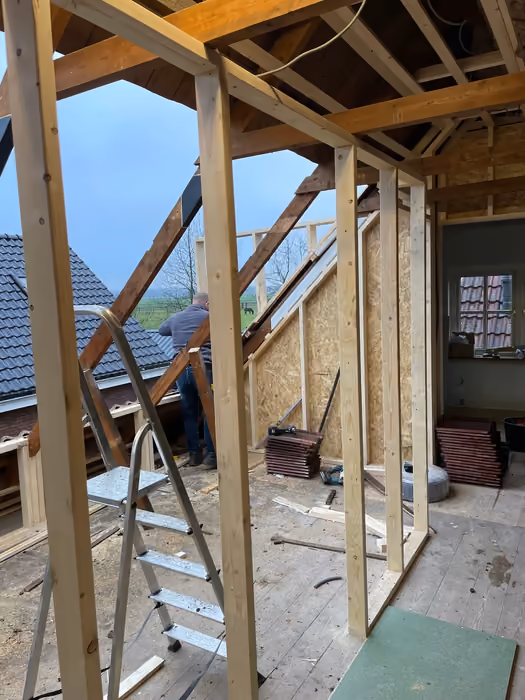 Zolder met houten regelwerk voor de dakkapel en een werkman op het dak