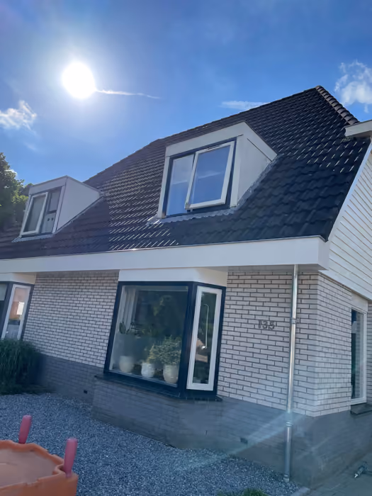 Woning met twee dakkapellen op donker pannendak in fel tegenlicht