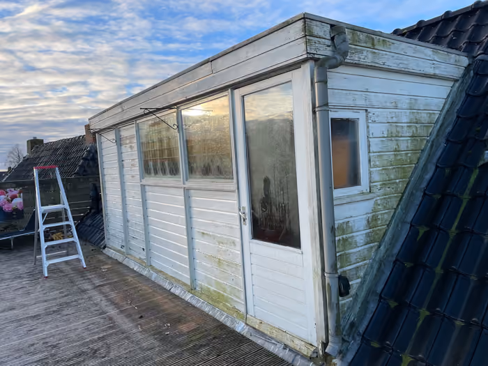 Oude witte houten dakopbouw met groene aanslag aan het dakterras