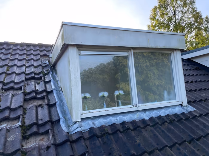 Oude dakkapel met verweerd houtwerk en zinken loodslabben op pannendak