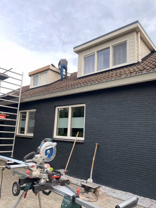 Timmerman op het dak bij twee nieuwe dakkapellen, afkortzaag op de voorgrond
