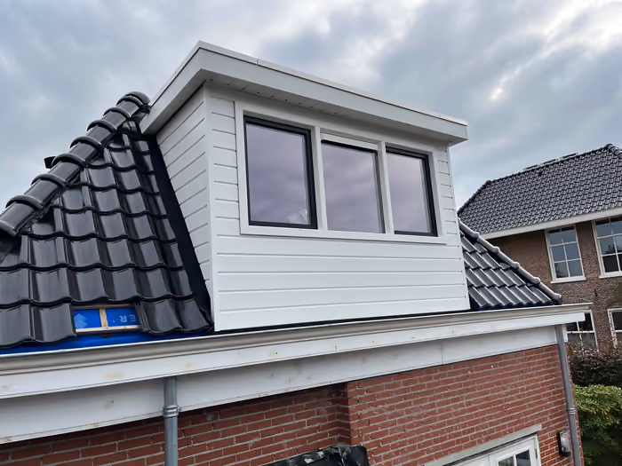 Nieuwe dakkapel met witte houten delen en donkere kozijnen op pannendak