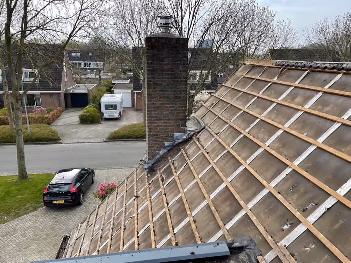 Kaal dakvlak met oude latten en dakbeschot, schoorsteen en straatzicht