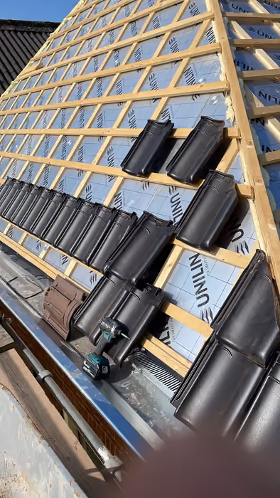 Stapels donkere dakpannen klaargelegd op panlatten boven isolatieplaten