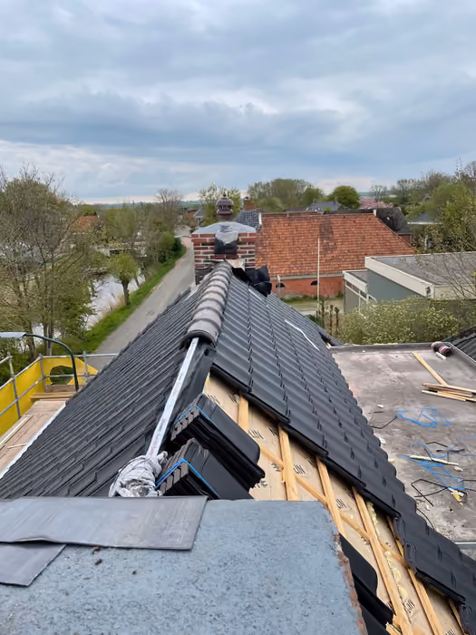 Nieuwe dakpannen en vorstpannen op de nok, met dorpsgezicht erachter