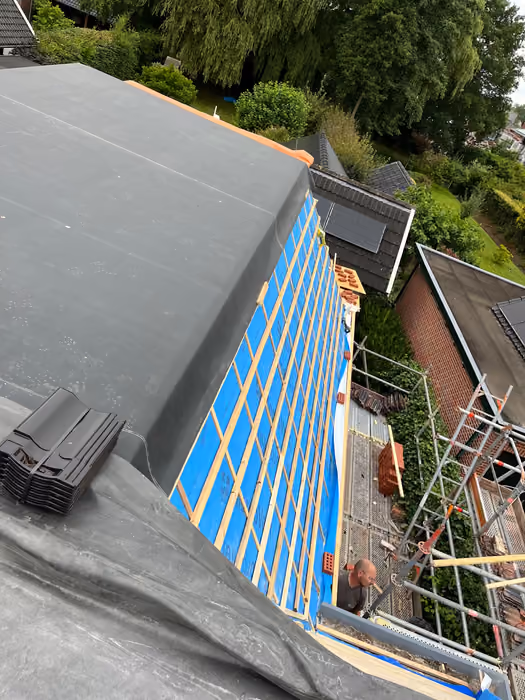 Schuin dakvlak met blauwe folie en panlatten naast een plat dak