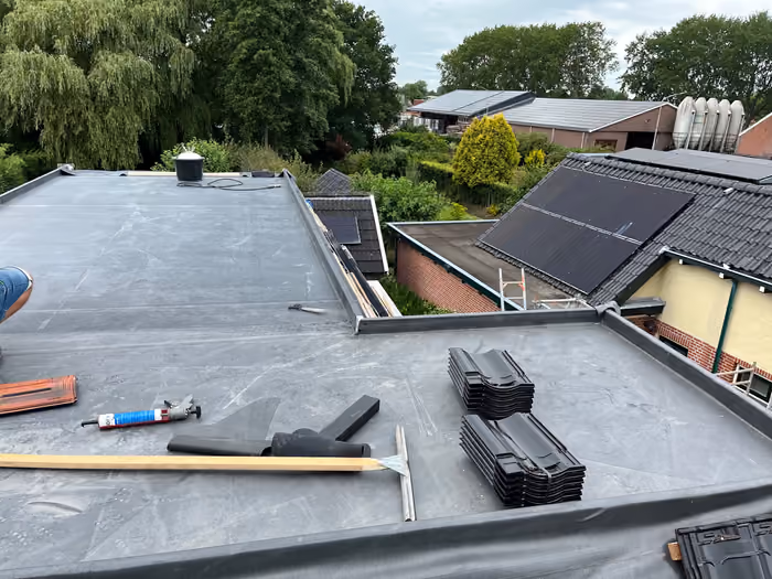 Plat dak met gereedschap en stapels dakpannen, uitzicht over de buurt