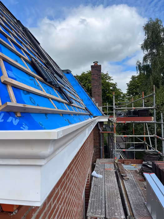 Dakvlak met blauwe onderdakfolie en panlatten, nieuwe witte goot en steiger