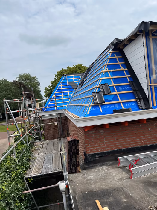 Dakvlak met blauwe folie, panlatten en ventilatiepannen naast een dakkapel