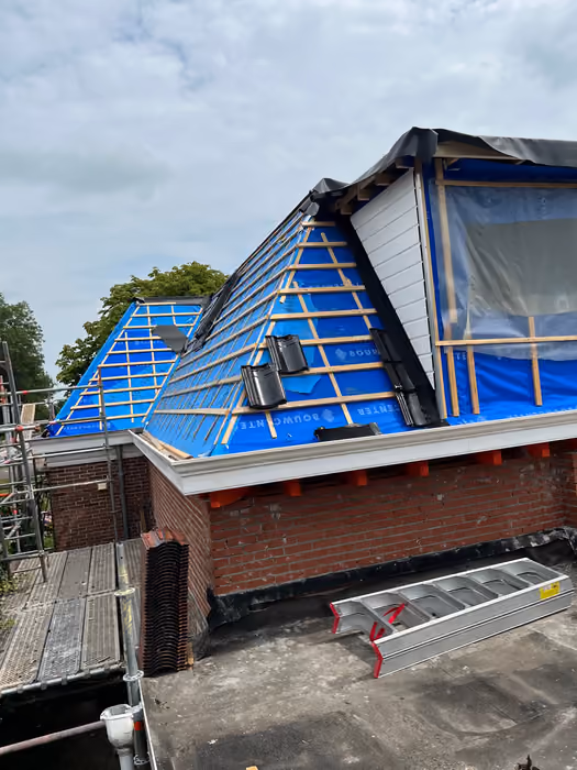 Dakkapel met witte betimmering naast een dakvlak met blauwe folie en panlatten