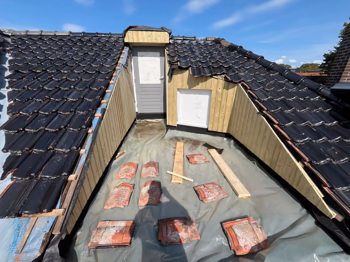 Ingebouwd dakterras met houten wandbetimmering en deur, vloer afgedekt met folie