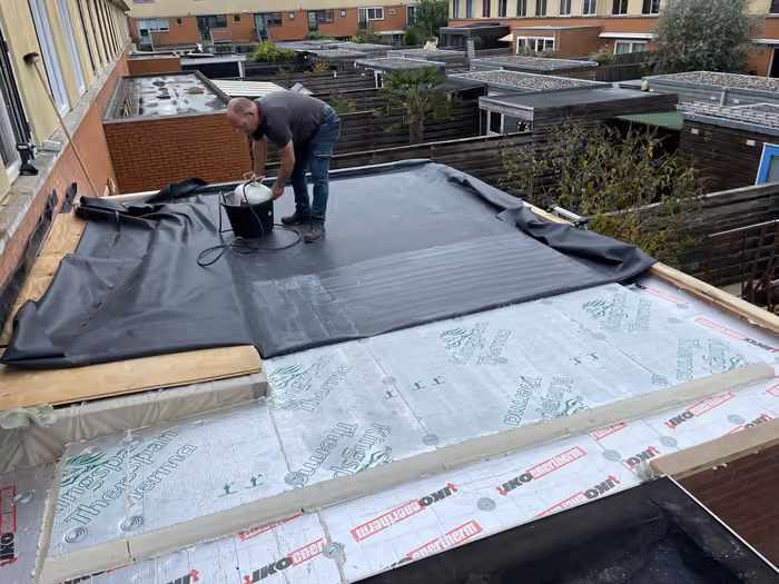 Man rolt zwarte dakbedekking uit over isolatieplaten op een plat dak