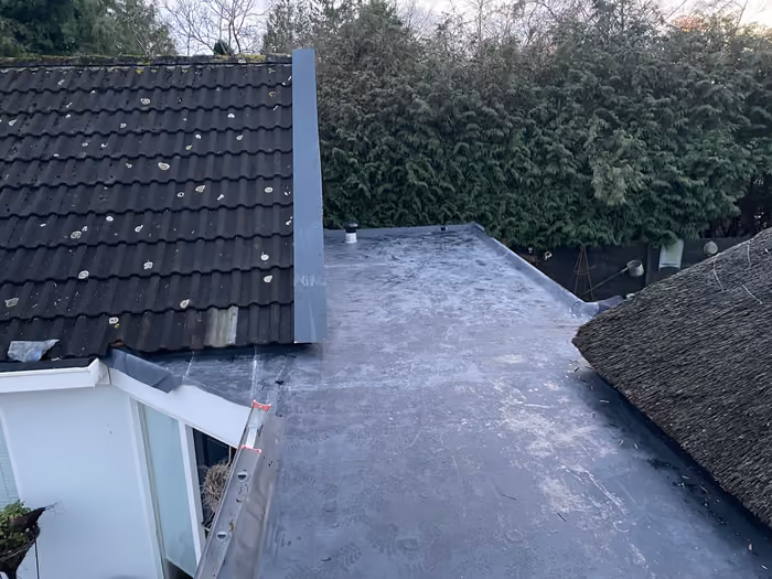 Afgewerkt plat dak met zinken muuraansluiting naast pannendak en rieten dak