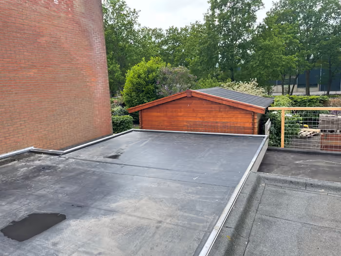 Afgewerkt zwart plat dak tussen bakstenen muur en houten tuinhuis met puntdak