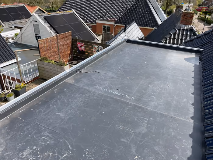 Nieuw plat dak met zwarte dakbedekking, uitzicht over pannendaken van de buurt