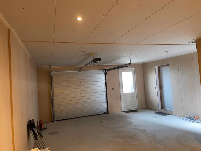 Garage van binnen met witte sectionaaldeur, loopdeur en afgewerkt plafond