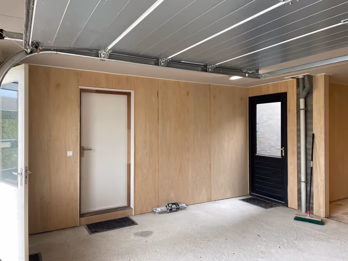 Garage-interieur met twee deuren, beplankte wanden en geopende sectionaaldeur