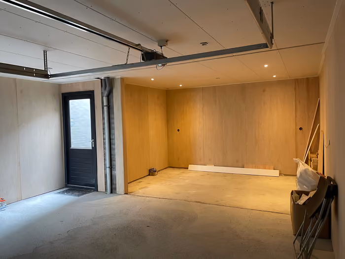 Garage met houten wandbeplating, donkere loopdeur en inbouwspots in het plafond
