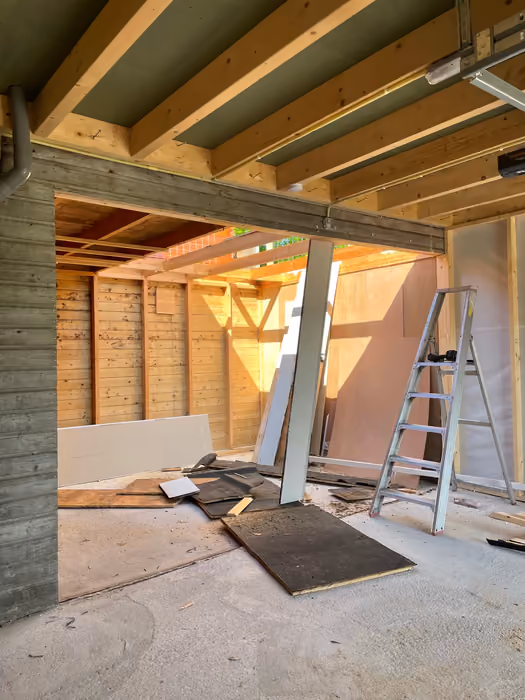Houten dakconstructie met balken en isolatie, ladder en plaatmateriaal op de vloer