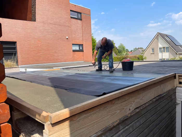 Man legt zwarte dakbedekking op een plat dak met houten randbalk