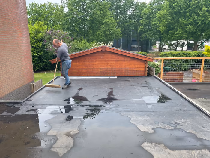 Man veegt regenwater van een nieuw plat dak met zwarte dakbedekking