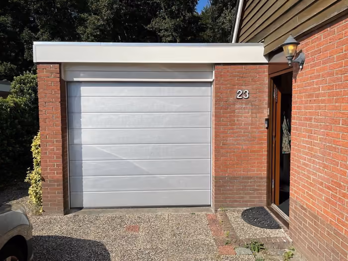 Nieuwe lichtgrijze garagedeur in gemetselde opening naast de voordeur van de woning