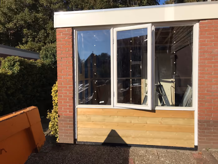 Aanbouw met witte kozijnen, glazen pui en houten gevelbekleding onder de ramen