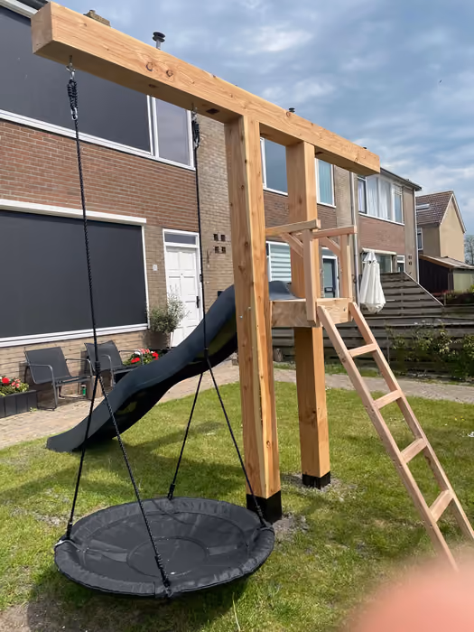 Houten speeltoestel met nestschommel, glijbaan en ladder in een achtertuin