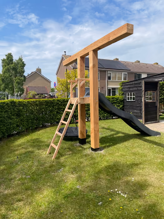 Houten speeltoren met glijbaan en ladder op het gazon onder blauwe lucht
