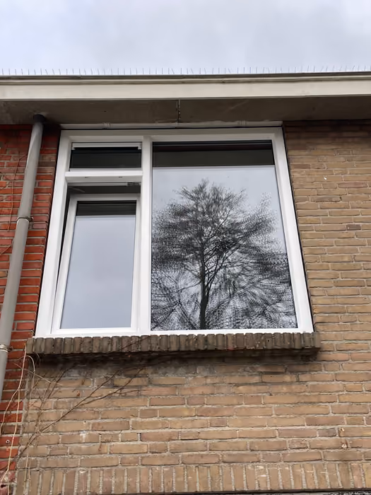 Nieuw wit kozijn met openstaand draaikiepraam in een bakstenen bovengevel