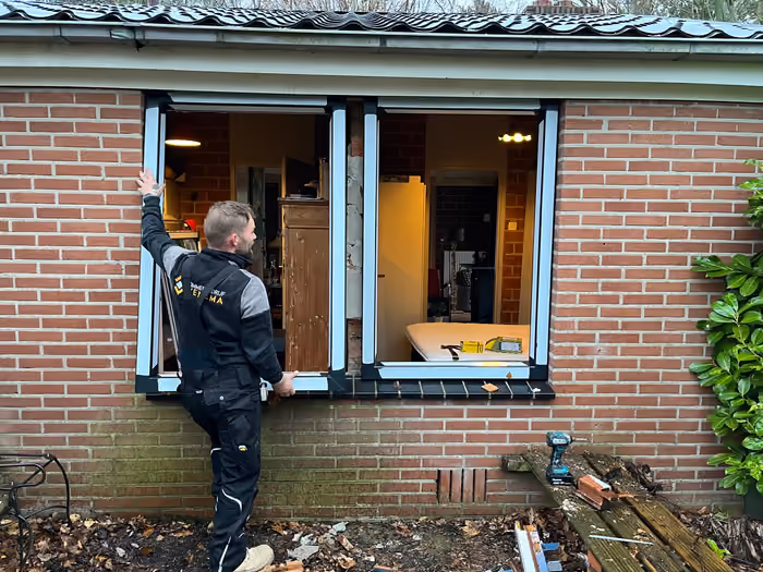 Timmerman verwijdert oude kozijnen uit de gevel van een bungalow