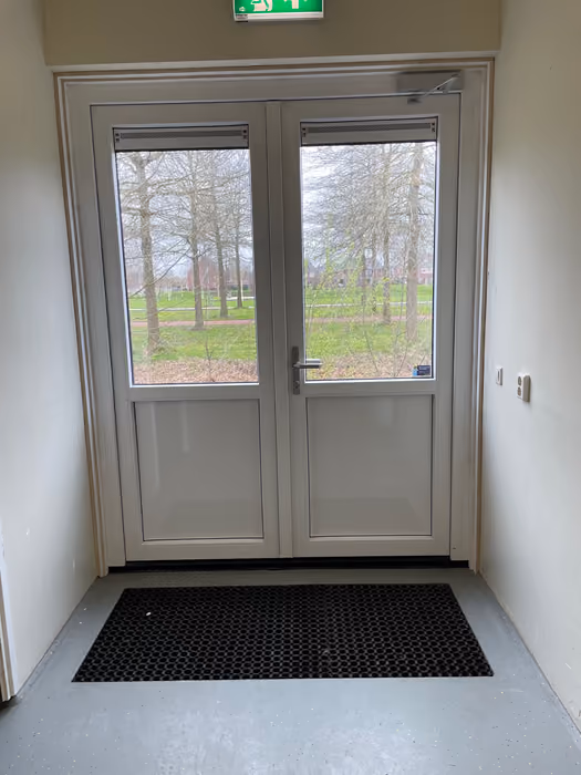 Witte dubbele kunststof deuren met glas in een hal, uitzicht op grasveld