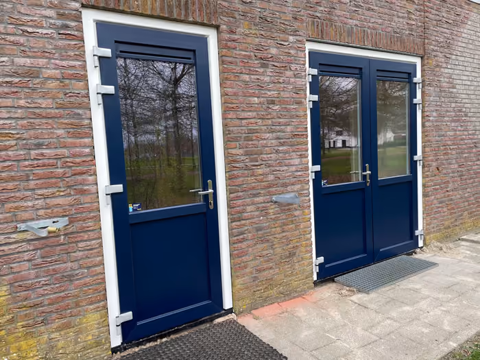 Donkerblauwe buitendeur en dubbele deuren met witte kozijnen in bakstenen gevel