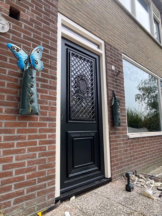 Zwarte voordeur met ruitmotief in het glas, schuin gezien vanaf de stoep