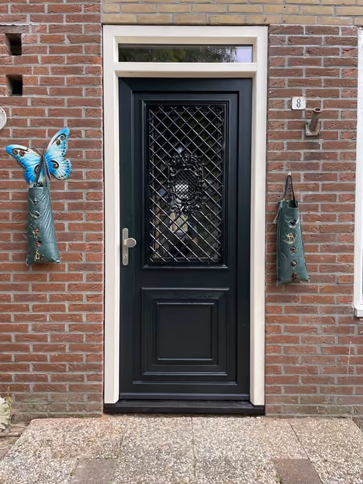 Zwarte voordeur met ruitmotief in het glas en bovenlicht in bakstenen gevel